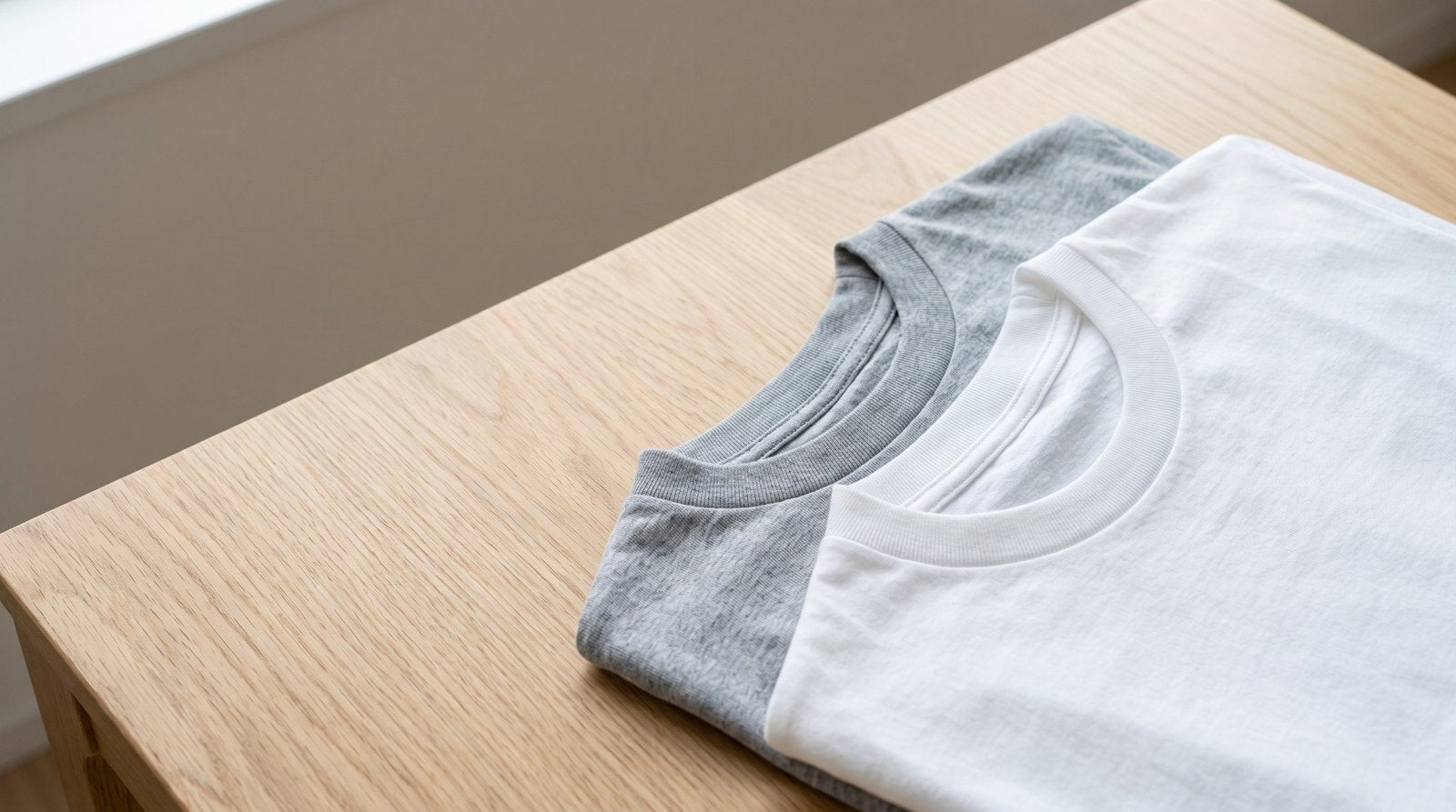 木のテーブルに並べたグレーと白の綿の無地Tシャツ