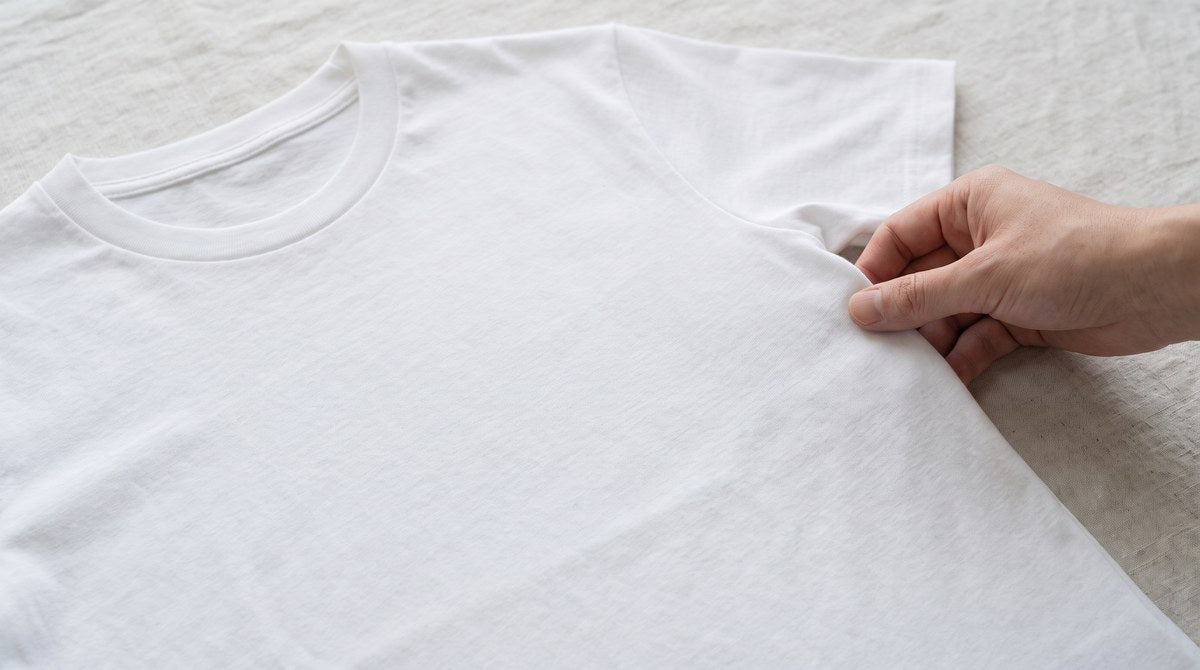 白い無地Tシャツを平置きにして、袖の付け根あたりに手を添え、脇に縫い目のない胴まわりを見せている写真